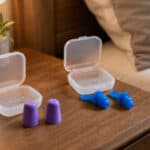 Foam and reusable flanged earplugs beside open storage cases on a bedside table.