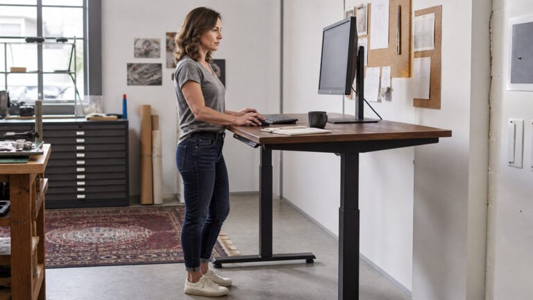 Woman working at an electric standing desk in a bright studio.