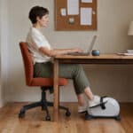 Woman working at a desk while using a compact pedal exerciser.